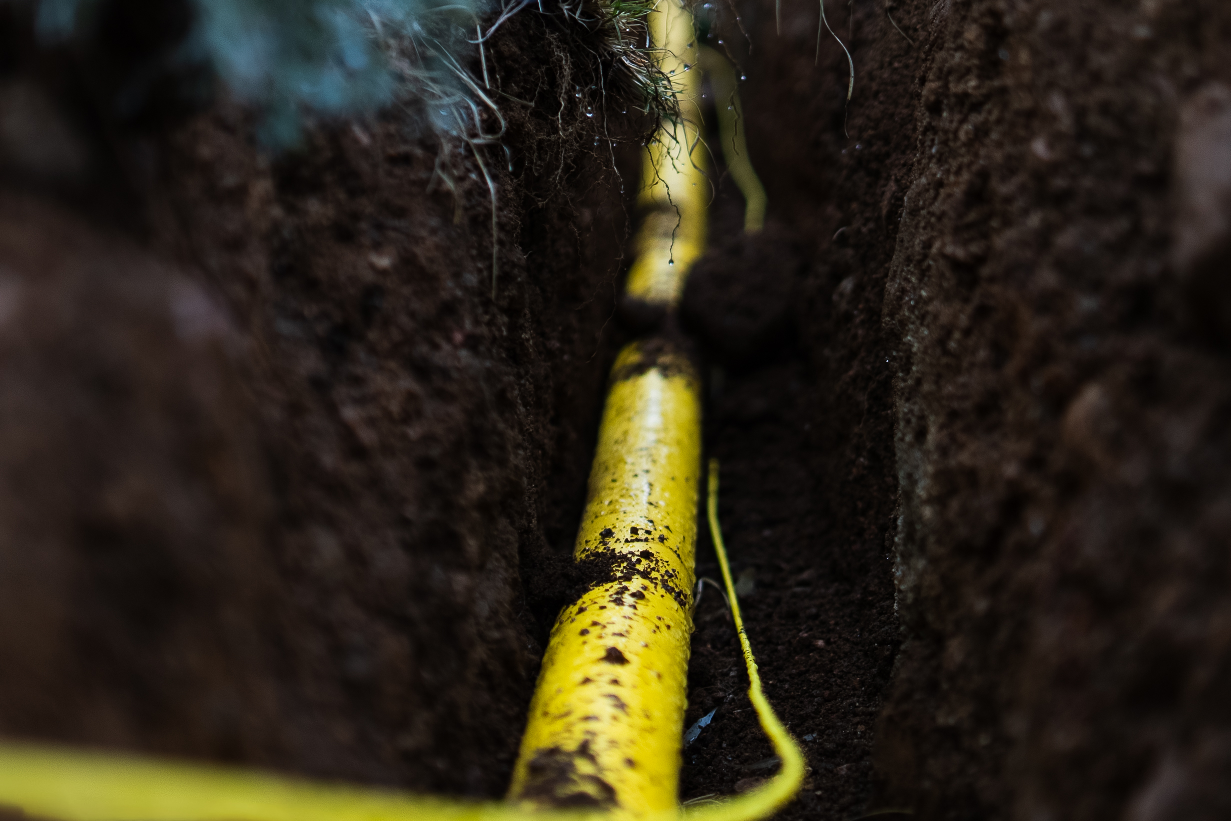 Close-up of yellow underground pipe inside a freshly dug trench